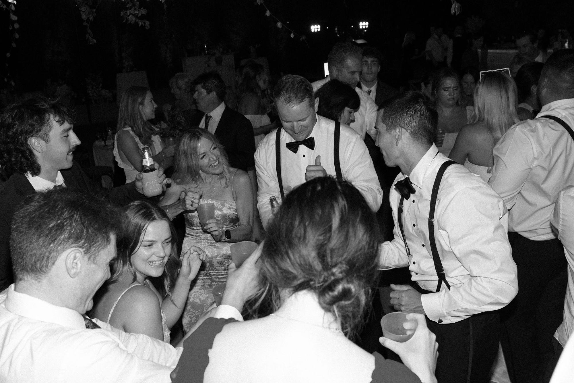 Wedding guests in black tie dancing and laughing on a crowded dance floor at night