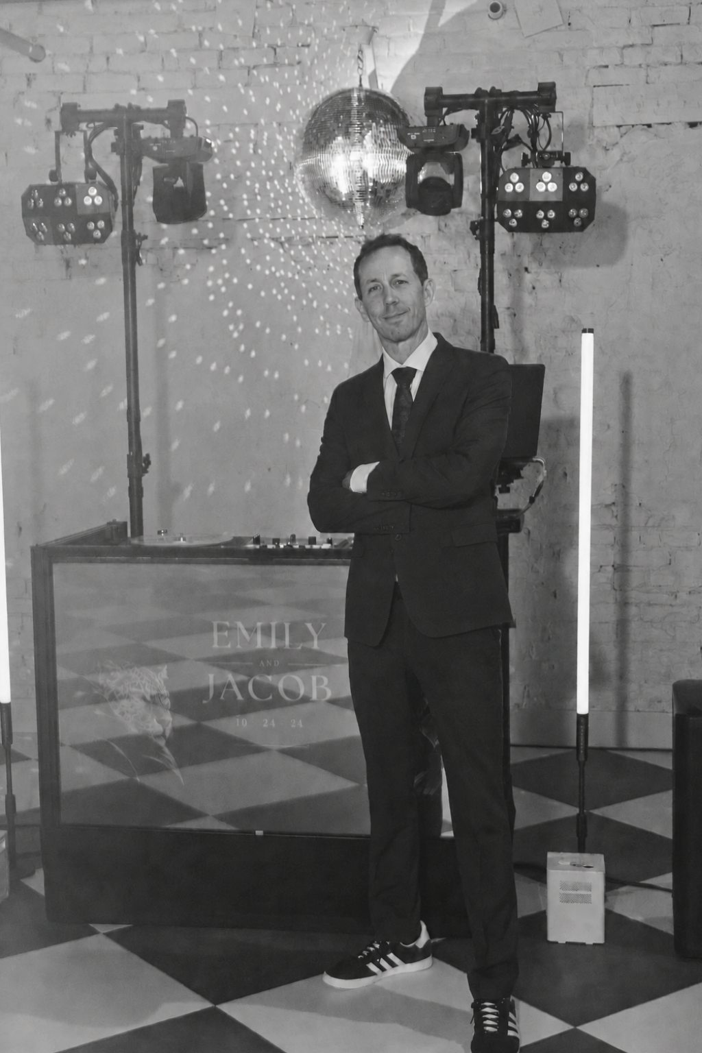 Matt in a dark suit, arms crossed, in front of his DJ booth and lighting rig